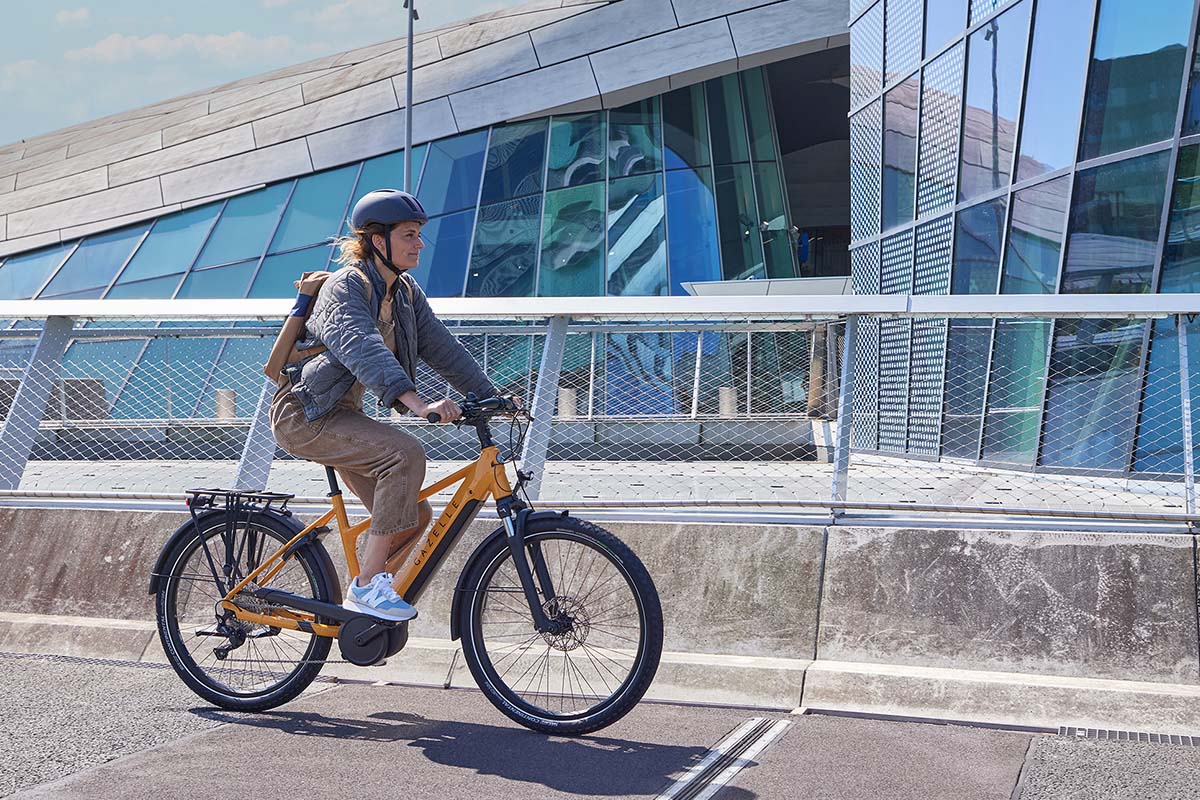 Frau fährt mit einem gelben E-Bike an einer Häuserfront entlang