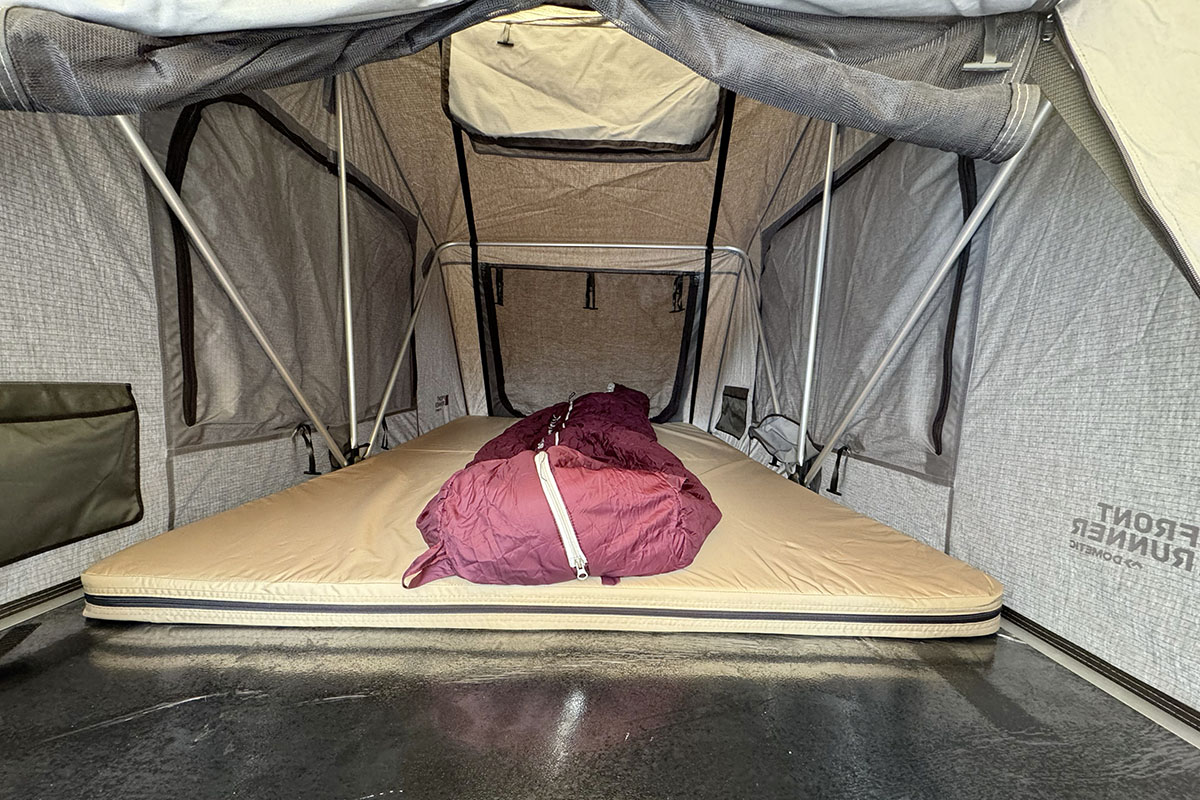Innenansicht in ein Dachzeltr mit ausgerolltem Schlafsack, der auf der Matratze des Zelts liegt.