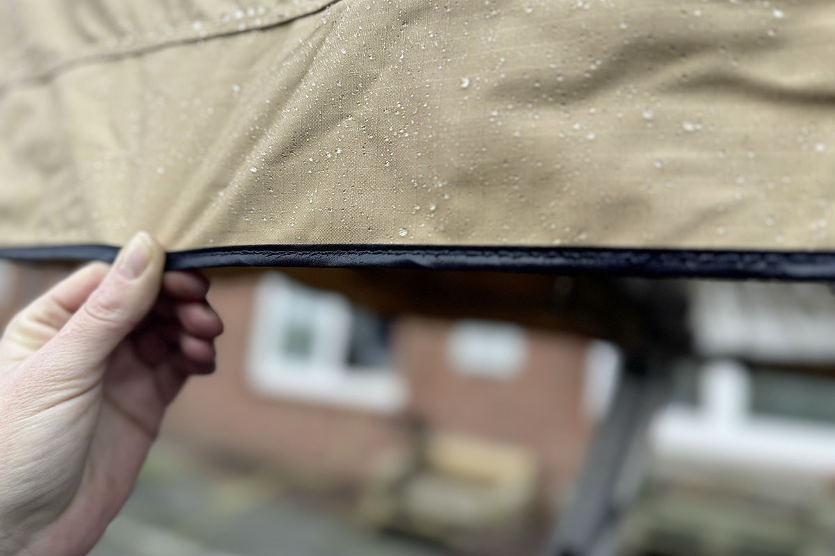 Detailansicht Dachzelt von Außen nach einem Regenguß tropft Wasser an der Zeltwand, die von einer Hand straff gehalten wird, herunter.