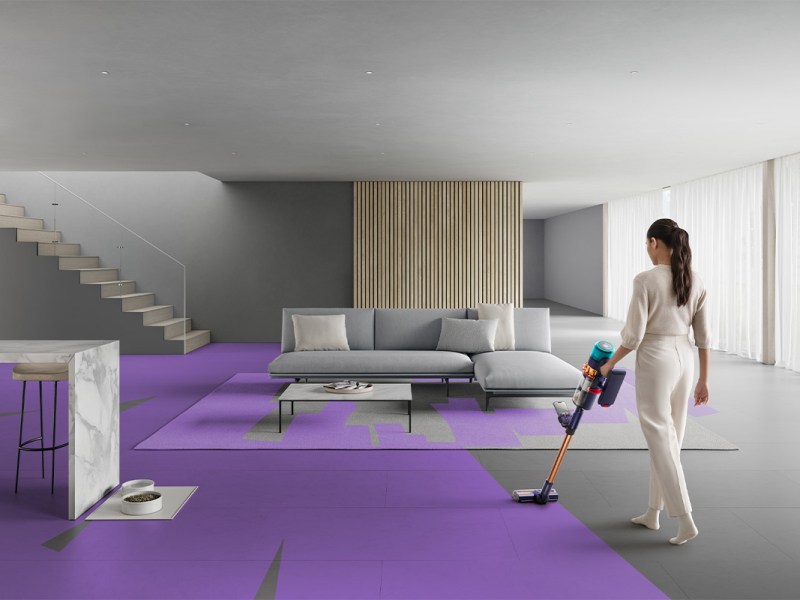 Eine Frau saugt mit einem Dyson-Akkusauger ein Wohnzimmer. In lila Streifen ist der Fortschritt des Putzens gezeigt.