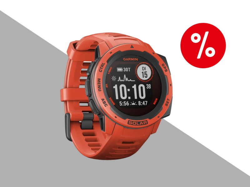 Garmin Instinct Solar in orange mit dunklem Display das digitale Uhr anzeigt schräg von vorne mit geschlossenem Armband auf hellgrau weißem Hintergrund mit rotem Prozentbutton oben rechts