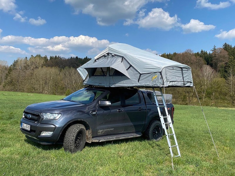 Dachzelt von Gordigear auf einem SUV montiert, der auf einer Wise vor einem Waldstück steht.