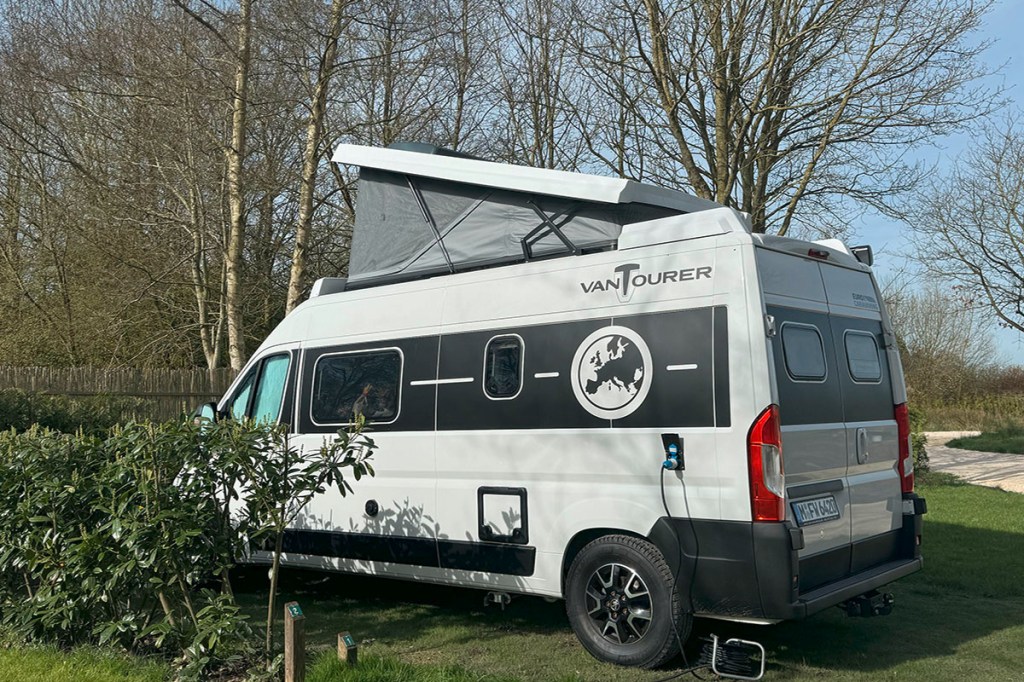 Camper-Van vom Mietportal CamperDays mit aufgestelltem Hochdach auf einer Wiese vor Wald.