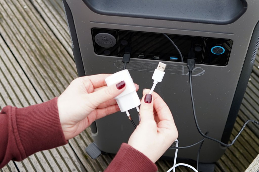 Zwei Hände halten ein Netzteil und ein USB-Ladekabel vor die Anker-Powerstation.