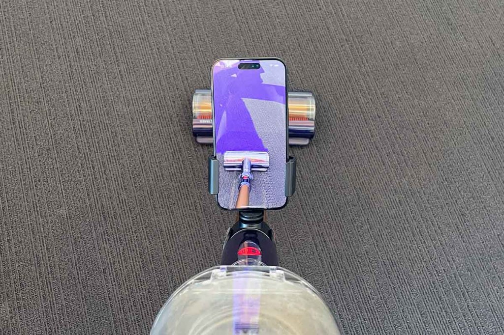 Ein Handy an einem Akkusauger von oben. Das Display zeigt den Boden mit lila Linien.