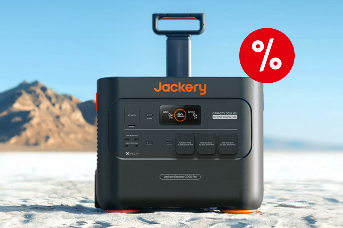 Schwarz orange Jackery Powerstation von vorne mit ausgefahrenem Griff auf weißem Sand vor blauem Himmel und Felsen im Hintergrund mit rotem Prozentbutton oben rechts