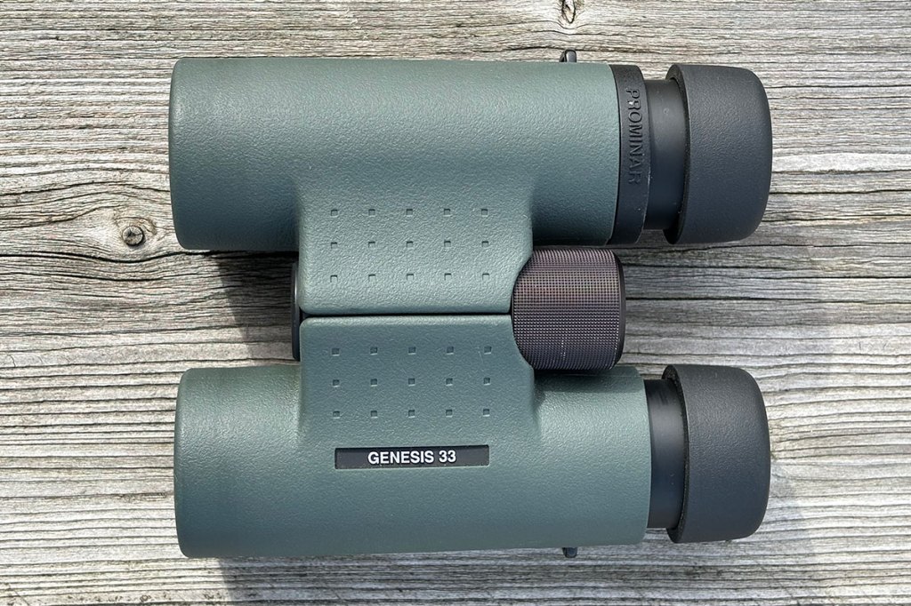Kowa Genesis Prominar 8x33 binoculars, shot from above, on a wooden table.