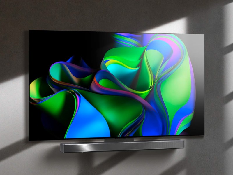 Fernseher mit bunten Farbwirbeln auf dem Display, an einer grauen Wand aufgehangen.