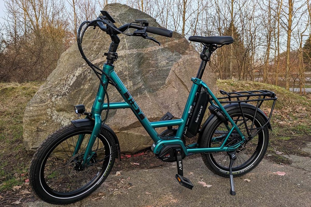 Totale eines grünen Kompakt-E-BIkes vor einem großen Stein stehend