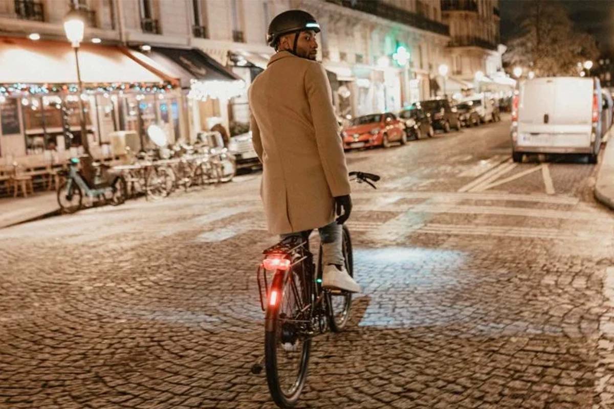 Mann fährt auf seinem Fahrrad durch eine nächtliche Stadt, man sieht ihn von hinten, er trägt einen Helm