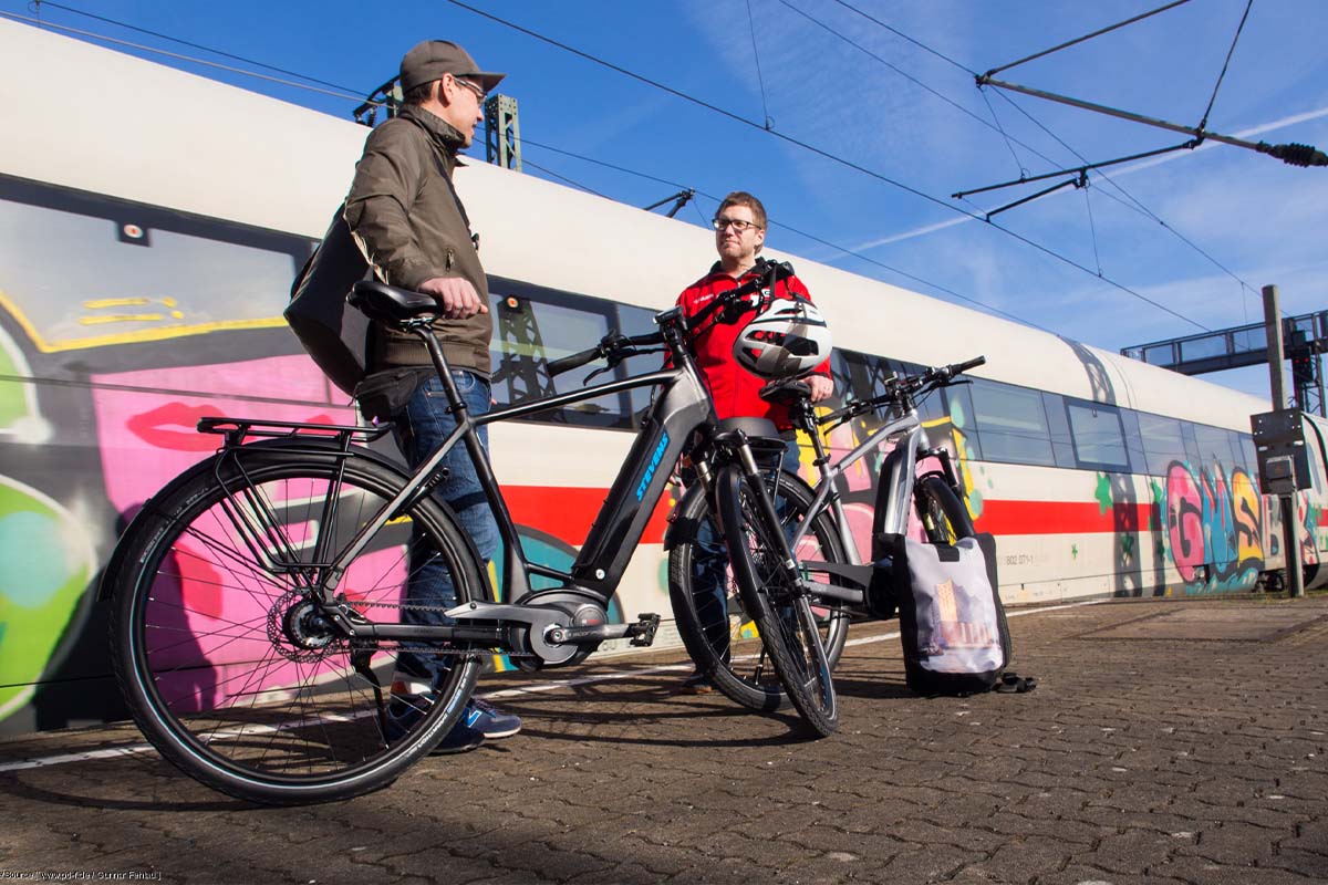 zwei Personen stehen mit ihren Fahrrädern am Bahnsteig, hinter ihnen ein ICE