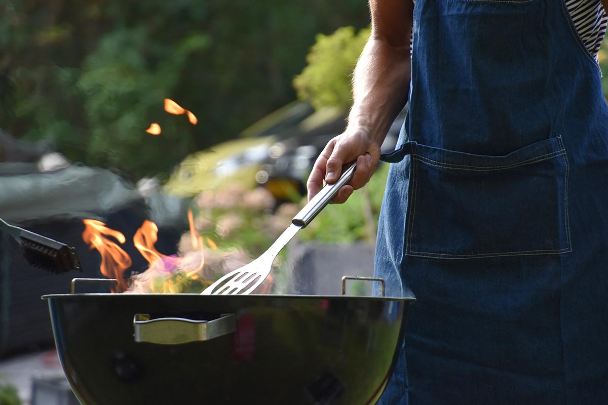 Person steht vor einem Grill unter freiem Himmel.