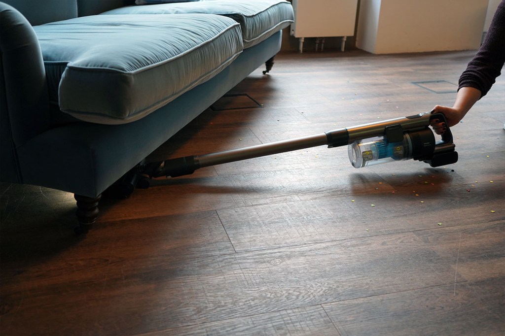 Eine Person saugt mit dem Philips-Akkusauger unter einem blauen Sofa.