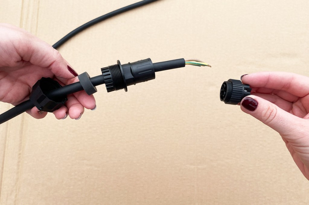 Zwei Hände halten das Kabel und die Bestandteile des zusammen zu bauenden Steckers.