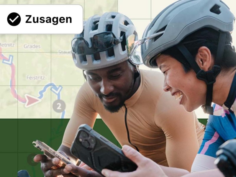 Zwei Personen mit Fahrradhelmen stehen nebeneinander und gucken auf ihre Smartphones, im Hintergrund ist eine Karte zu sehen.