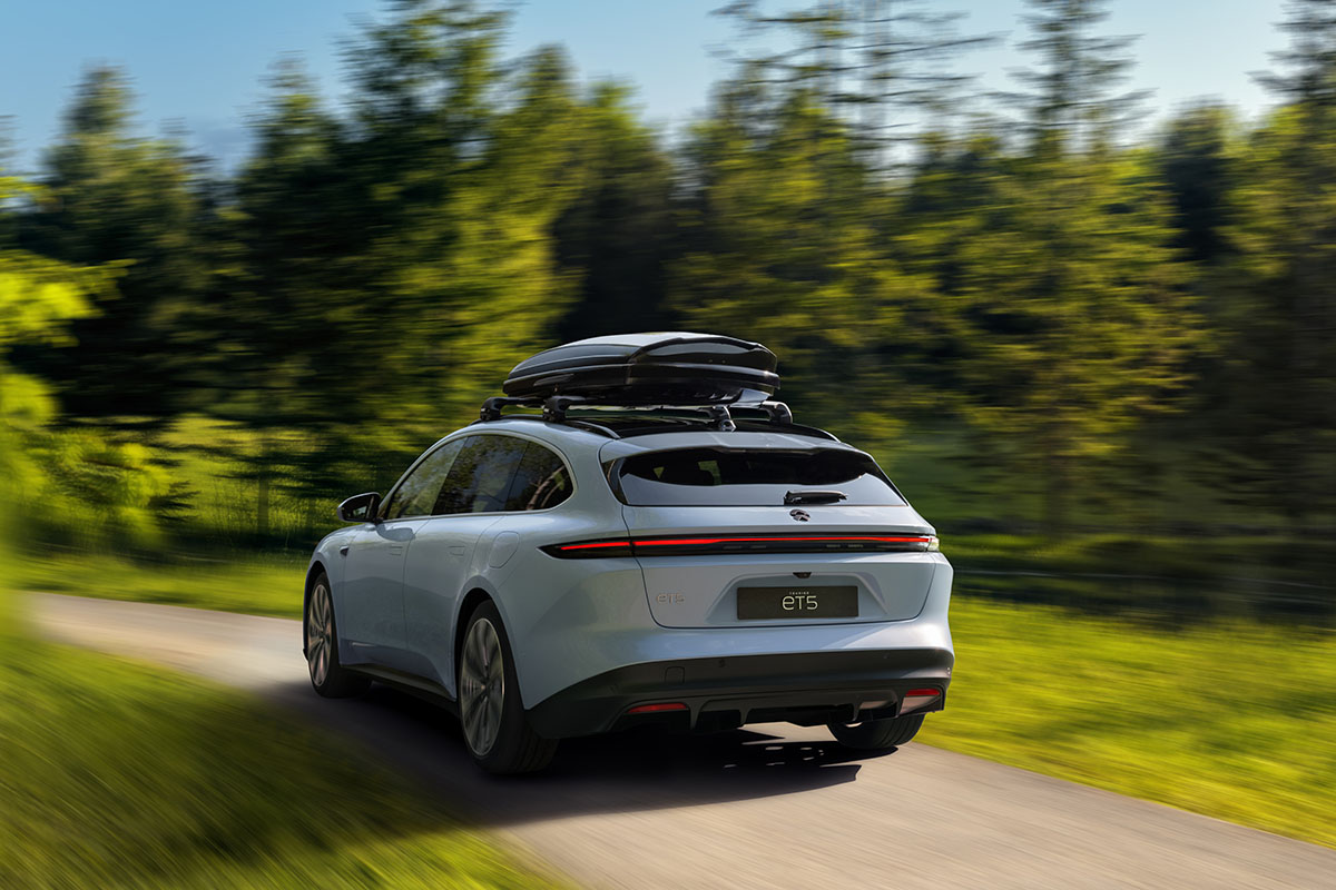 E-Auto Nio ET5 Touring fährt durch eine Waldlandschaft. Zu sehen ist der E-Kombi von hinten. Eine Dachbox ist auf dem Autodach befestigt.