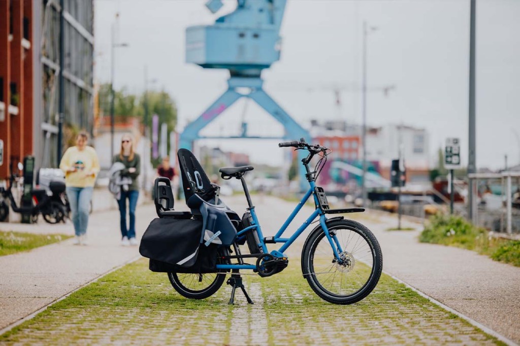 Kompaktes E-Lastenrad steht vor einem alten Industriekran auf einer Promenade