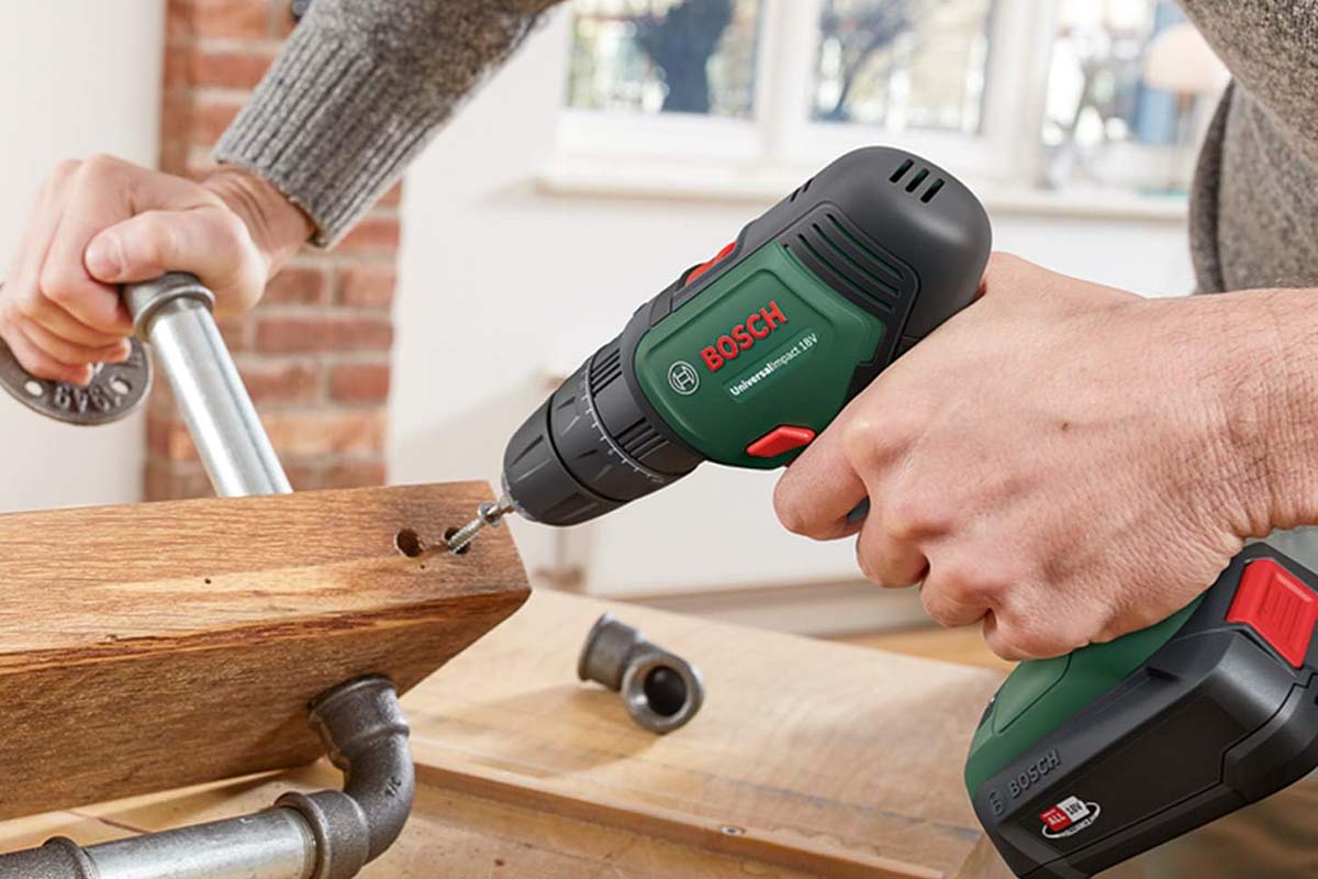 Hand hält ein Holzstück mit Rohren fest, eine andere einen Bohrer