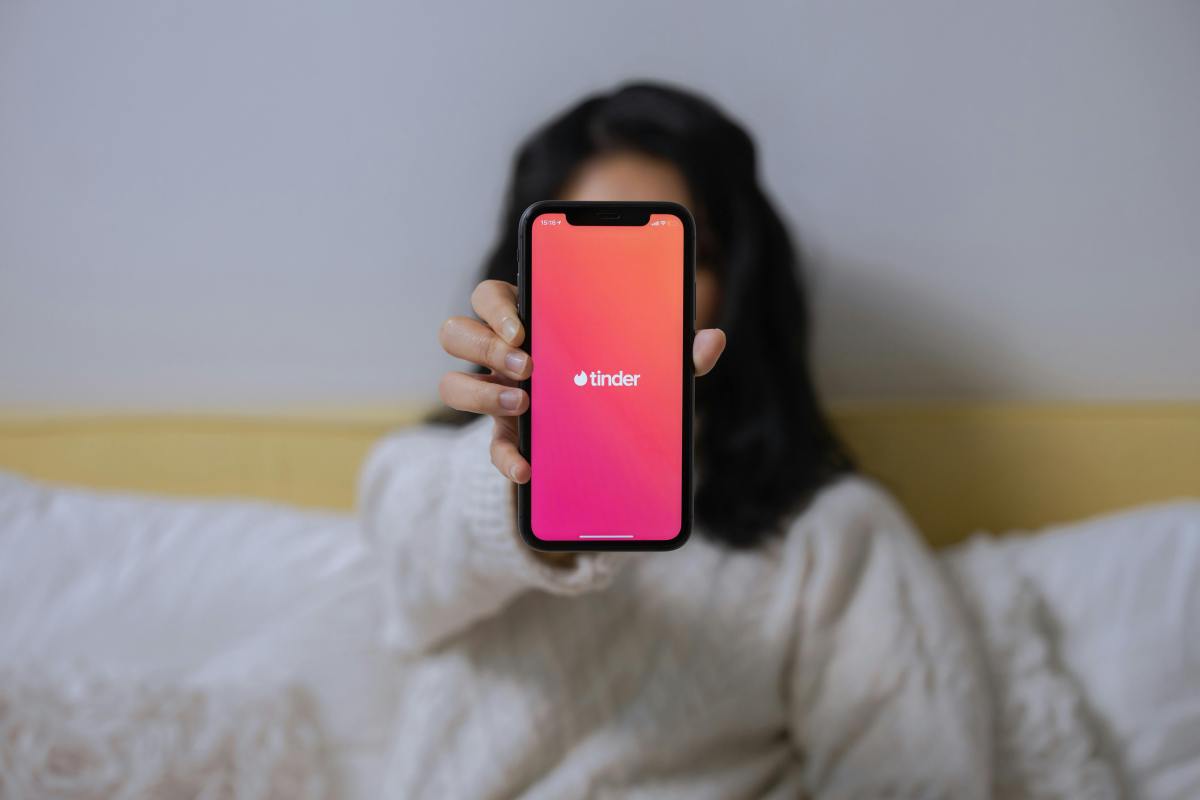 Eine Frau hält ein Smartphone mit der Tinder-Startseite in die Kamera.