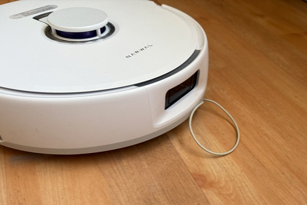 Der Narwal Freo Z10 auf Laminat mit einem Kabel, das unter dem Gehäuse verschwindet.