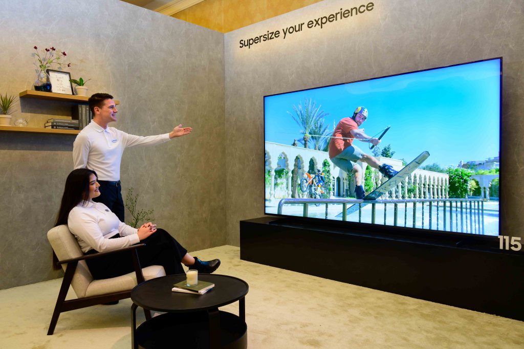 Zwei Personen schauen begeistert auf einen großen Samsung-Fernseher, der einen Skateboarder zeigt.