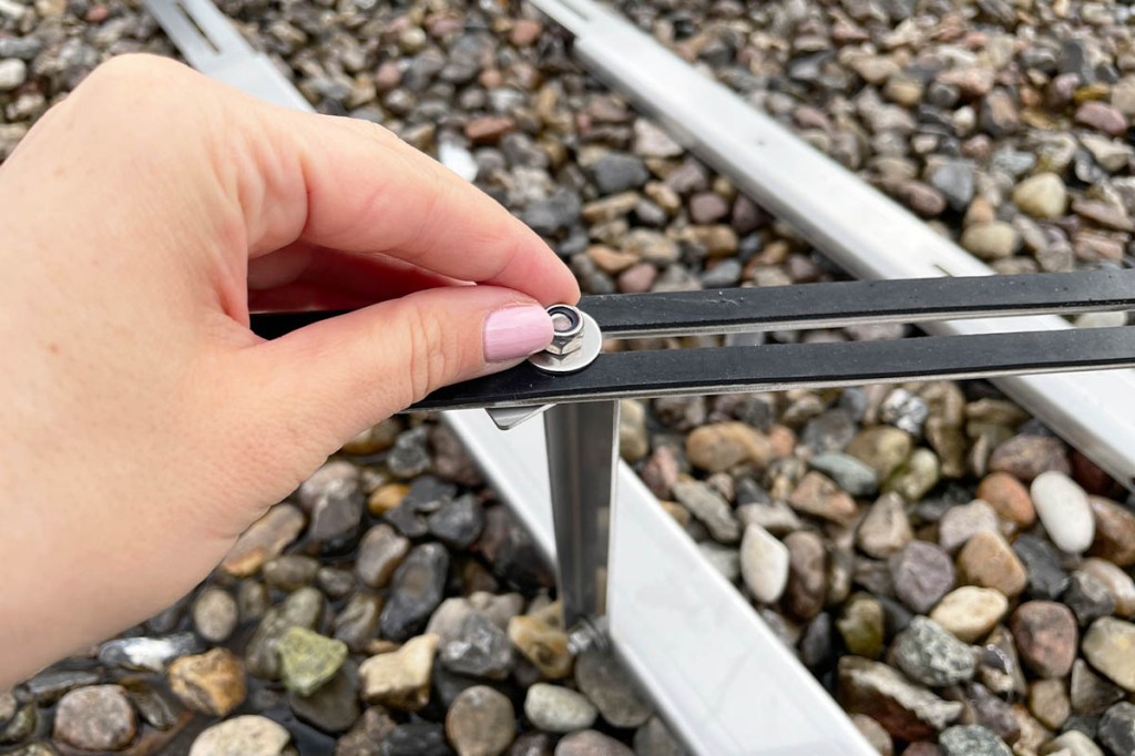 Eine Hand schraubt an einer Halterung aus Metall.