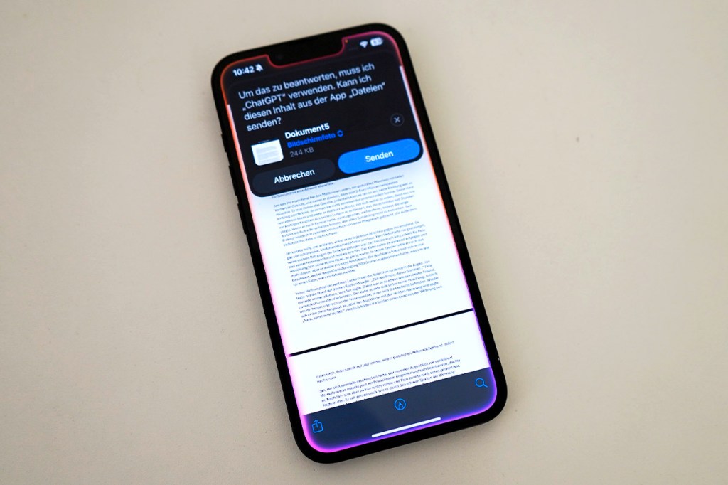 Ein iPhone liegt auf einem Tisch. Auf dem Bildschirm wir ein Text mit Hilfe von Apple Intelligence zusammengefasst.