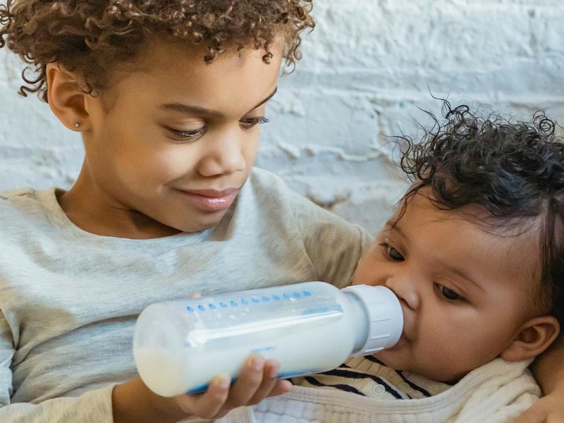 Ein Kind gibt einem Baby die Flasche