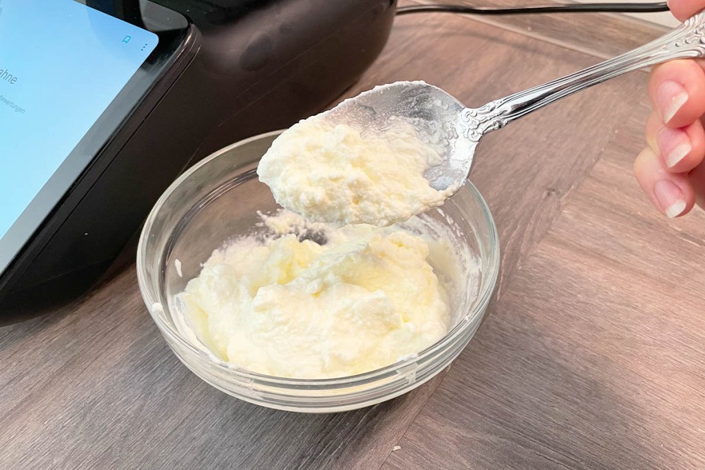 Eine Schüssel mit Schlagsahne, ein Löffel hebt einen Teil heraus.