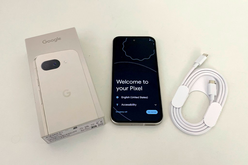 Das Pixel 9a liegt neben der Verpackung und den mitgelieferten Ladekabel auf einem weißen Tisch.