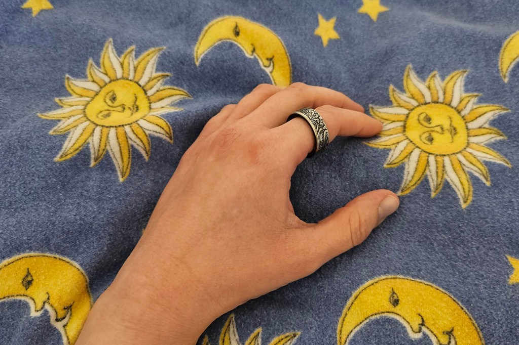 Smart Ring an einer Hand auf einer Bettdecke