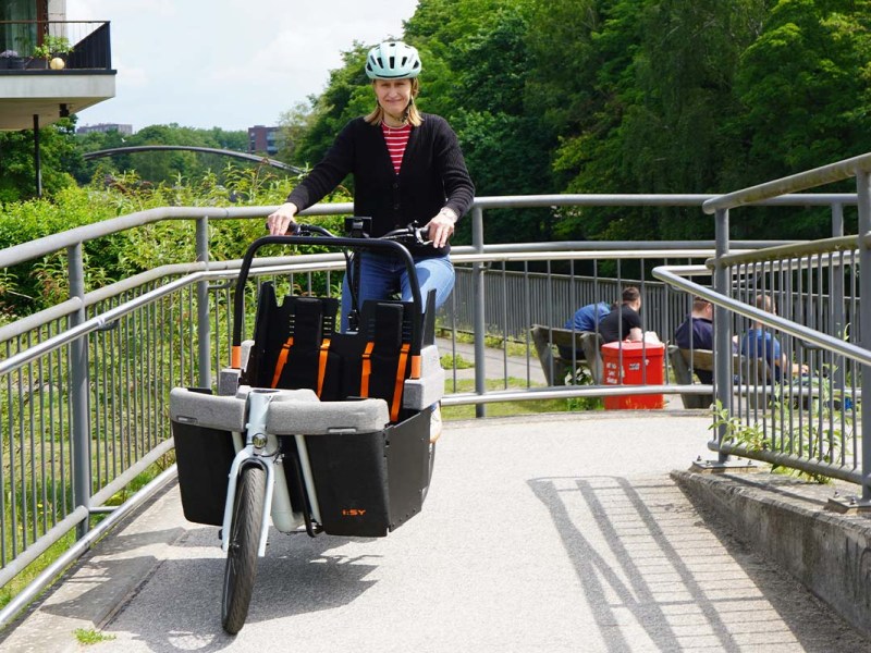 Frau fährt mit einem Cargo-E-Bike über eine Brücke