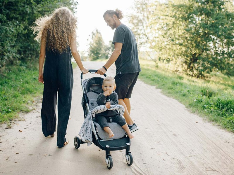 Mann und Frau gehen einen Feldweg entlang und ziehen einen Buggy hinter sich her, in dem ein Kind sitzt