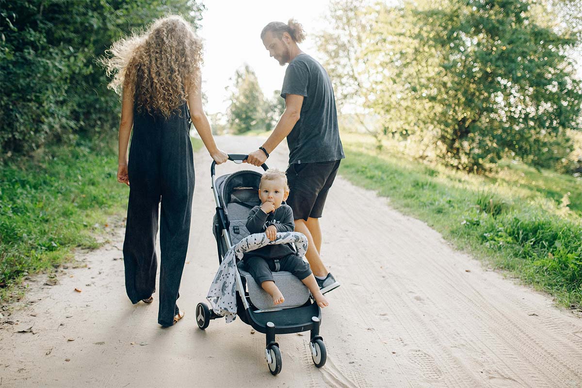Mann und Frau gehen einen Feldweg entlang und ziehen einen Buggy hinter sich her, in dem ein Kind sitzt