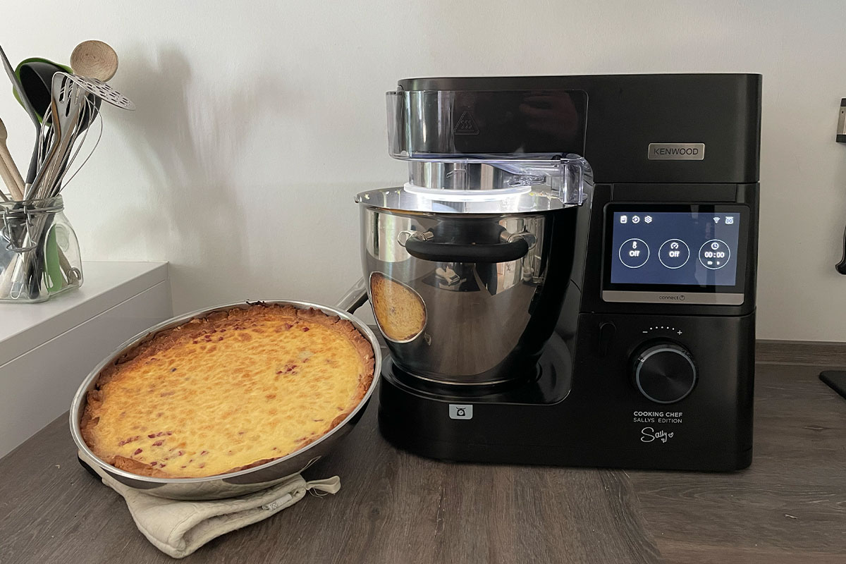 Der eingeschaltete Kenwood Cooking Chef in der Sallys Edition auf einer Küchenarbeitsplatte. Daneben steht eine Quiche.