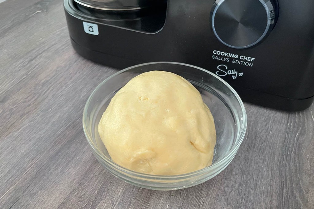 Eine Kugel Mürbeteig in einer Glasschüssel auf einer Arbeitsplatte. Im Hintergrund der Kenwood Cooking Chef Sallys Edition.
