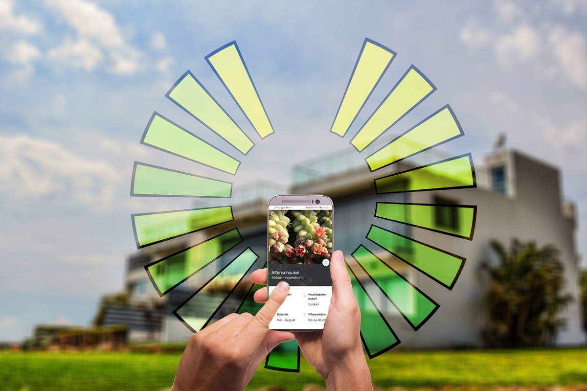Eine Hand mit Smartphone vor einem Haus