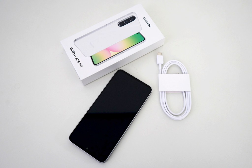 Das Mittelklasse-Smartphone Samsung Galaxy A56 5G liegt neben der Verpackung und dem mitgelieferten ladekanel.