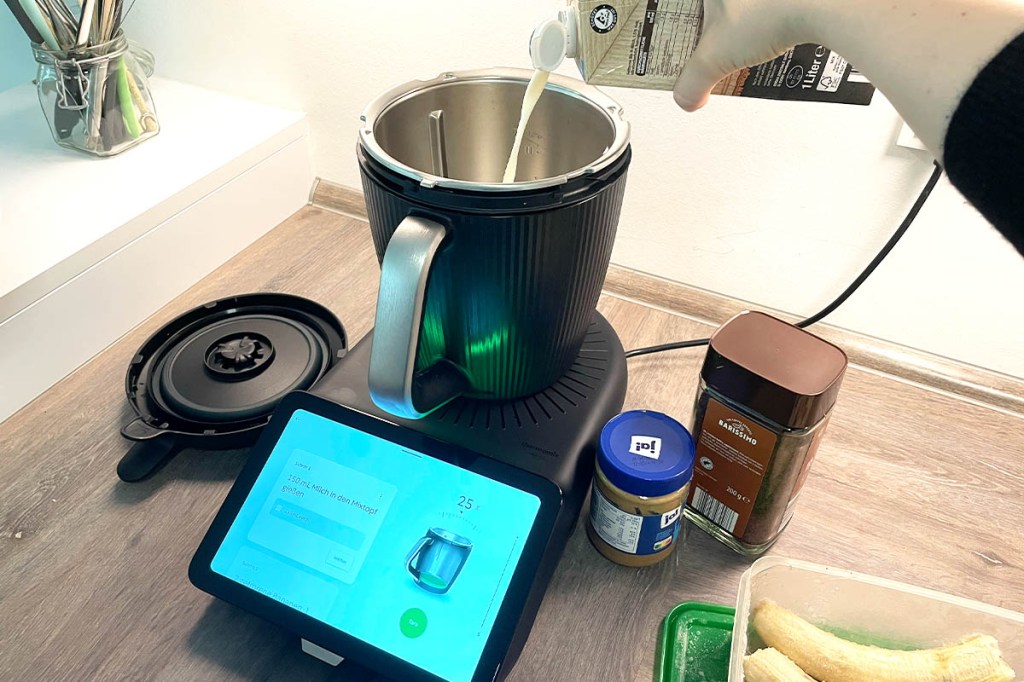 Eine Person gießt Milch in den Thermomix TM7. Daneben weitere Zutaten.