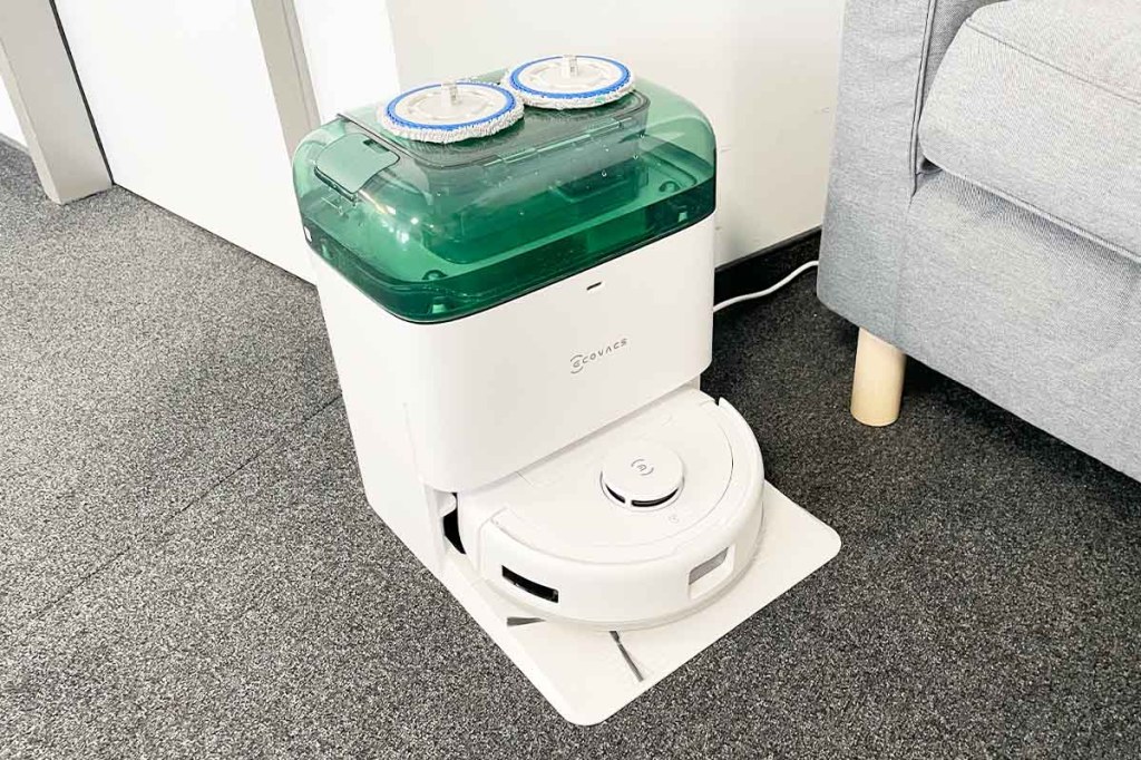 Der Deebot mini in seiner Station in wohnlicher Umgebung. Die Wischblätter liegen oben auf dem Wassertank.