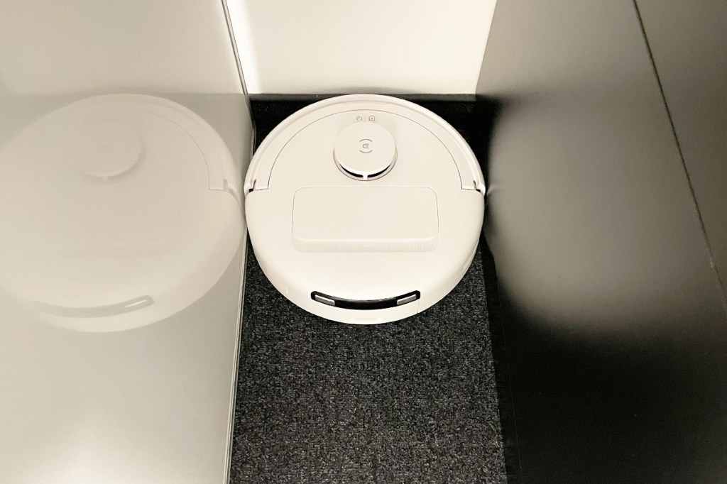 Der Deebot mini in einer schmalen Lücke zwischen Möbeln.