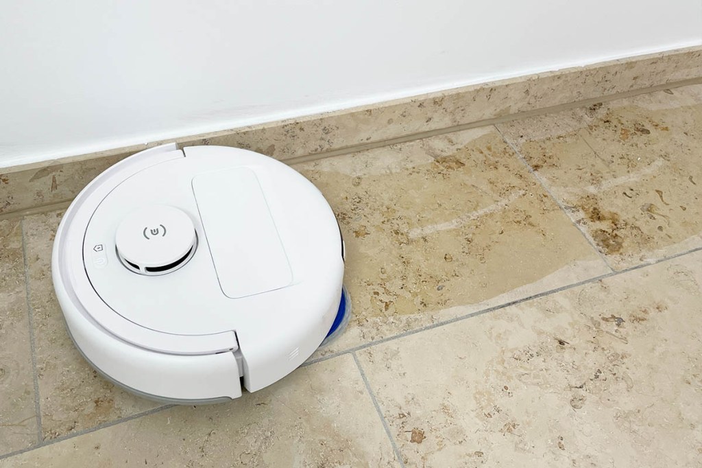 Der Deebot mini wischt auf hellem Steinboden an einer Wand lang. Die Wasserspuren sind zu sehen.