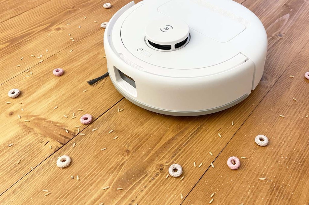 Der Deebot mini auf Holzfußboden mit buntem Schmutz drum herum.