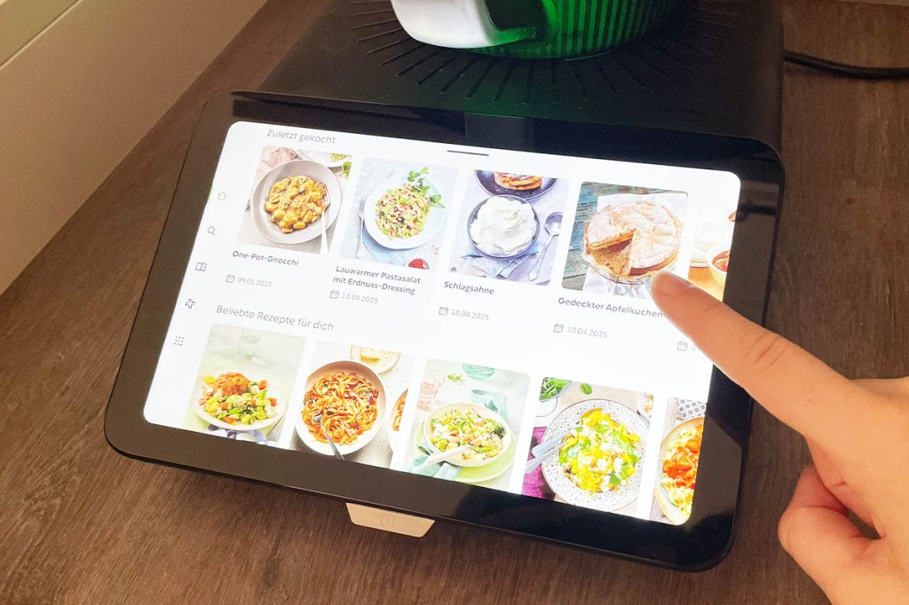 Eine Hand bedient das Display des TM7, auf dem Rezepte mit Bildern zu sehen sind.