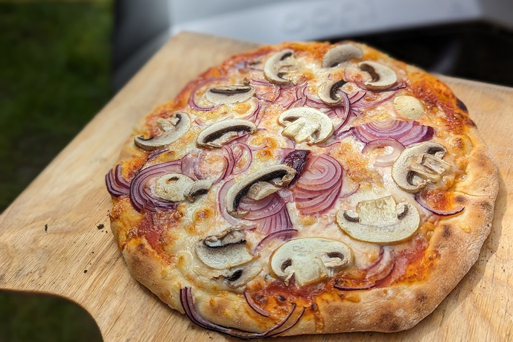 Einew fertige Pizza mit Zwiebeln und Champignons vom elektrischen Pizzaofen