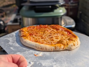 Eine fertige Pizza aus dem Gozney vs. Cozze-Duell mit Pizzaofen im Hintergrund 