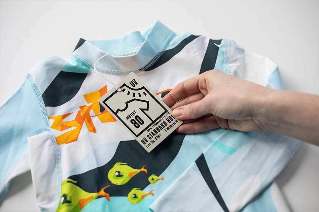 Nahaufnahme T-shirt, eine Hand hält das Etikett in die Kamera