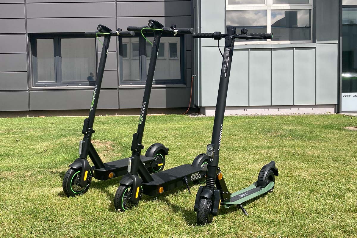 drei E-Scooter vor einem Firmengebäude auf einer Wiese stehend
