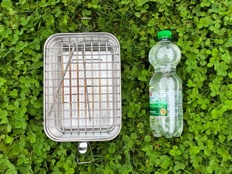 Grill und eine Wasserflasche liegen nebeneinander auf einer Wiese