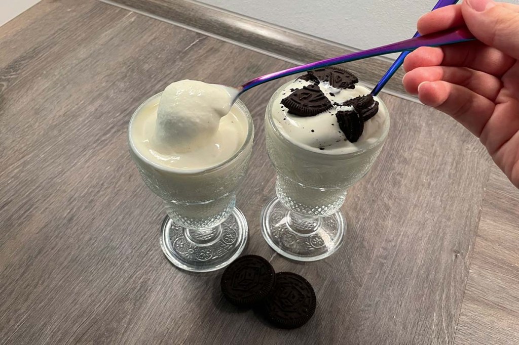 Mit einem langen Löffel wird das etwas flüssige Vanille-Softeis aus einem Glas gelöffelt.